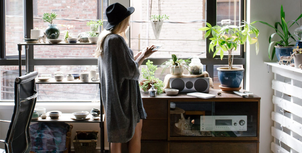 A woman gazes at plants by a window, providing solace during extended periods spent at home.