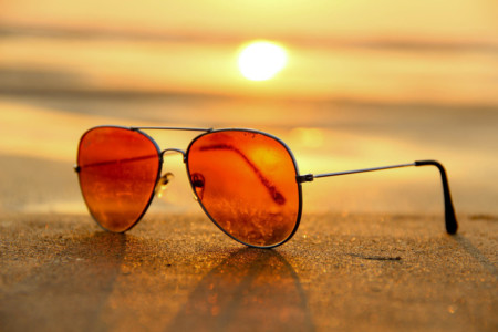 A pair of sunglasses on the sand at sunset, symbolizing summer.