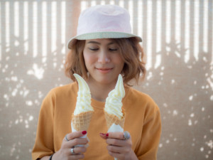 A woman wearing a hat having summertime ice cream fun with two cones.