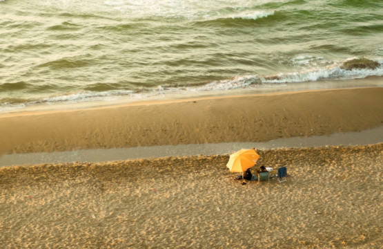 Two people sitting on a beach under an umbrella.