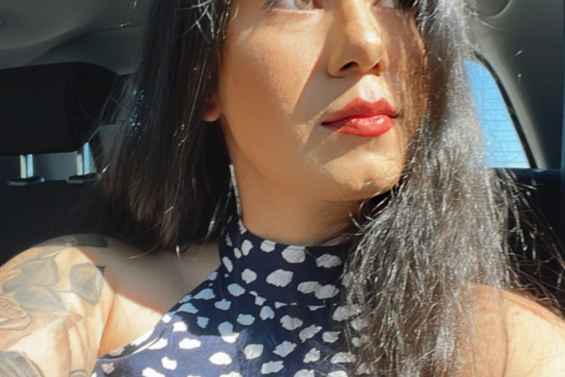 A woman with tattoos sitting in the back seat of a car on the 18th floor.