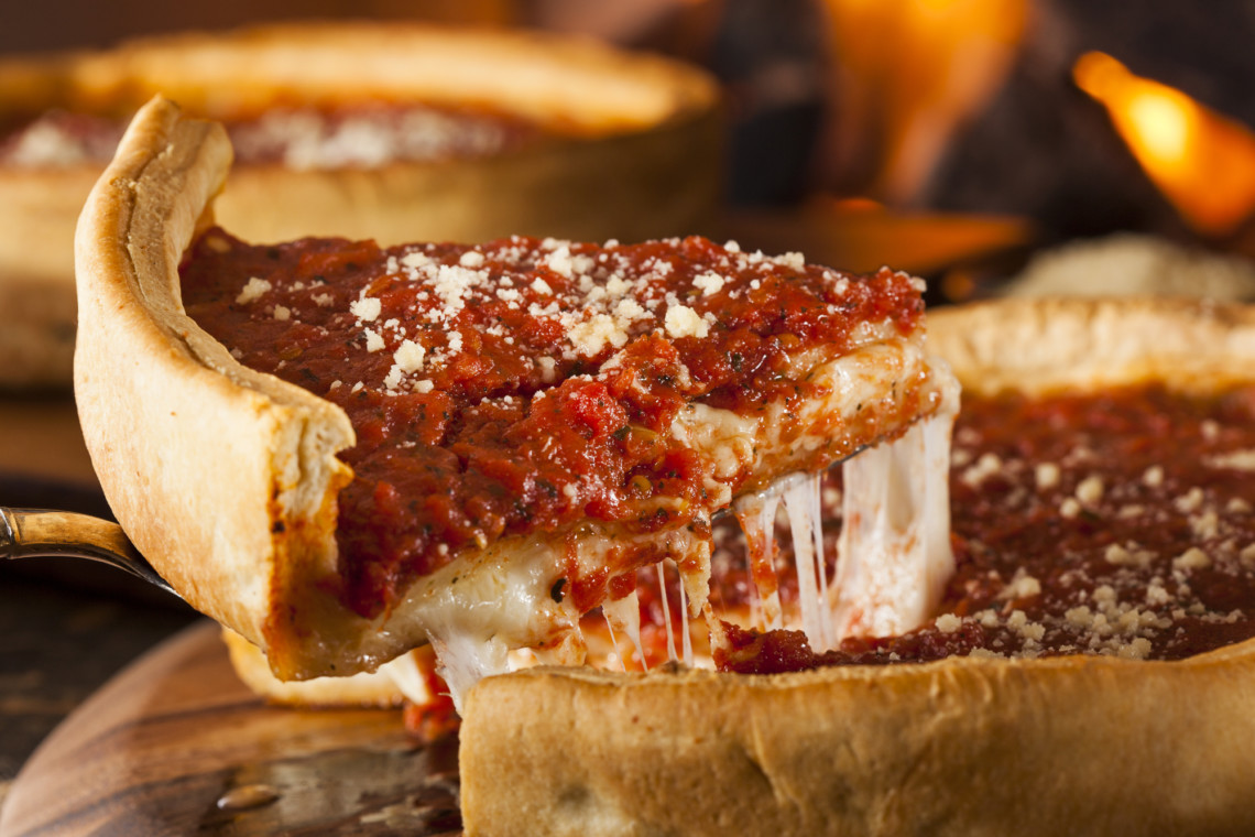 A slice of deep dish pizza is being taken out of a pan at a pizza day party.