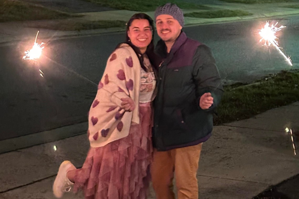 Two individuals holding sparklers on a sidewalk, featured in the Resident Spotlight: Isabella F. and Gabriel E. on the 13th floor.