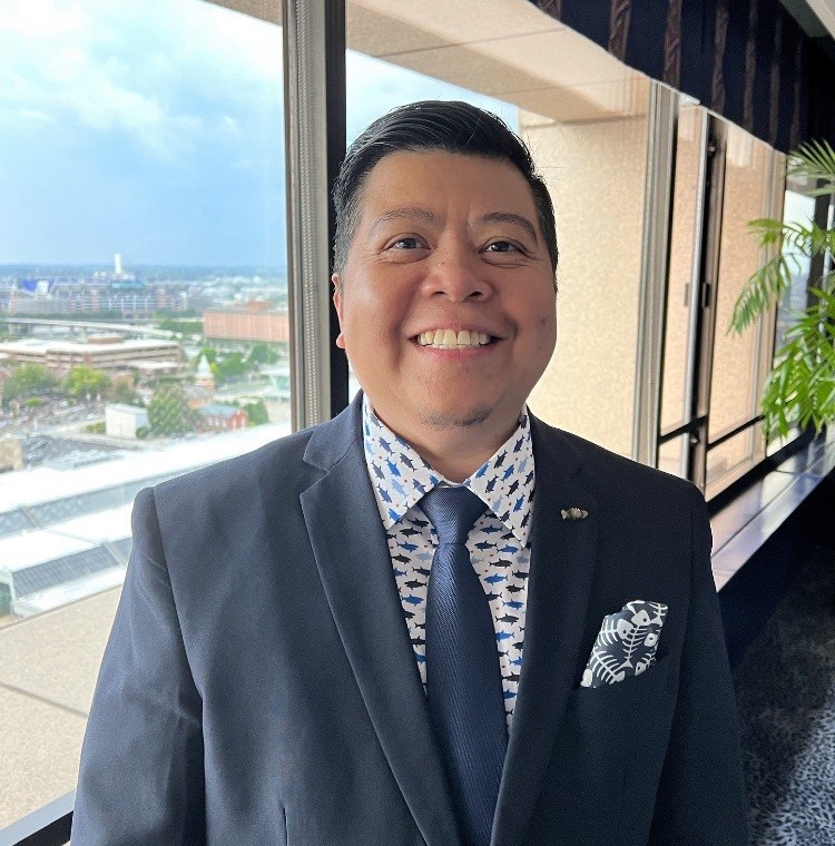 A man in a suit standing in front of a window on the 16th Floor.