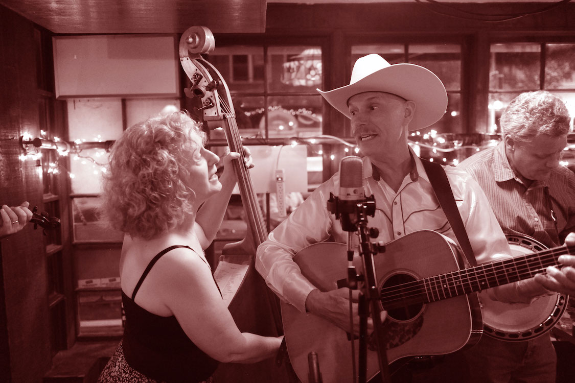 A man in a cowboy hat playing an acoustic guitar at Music In The Courtyard - Blue Spruce Bluegrass.