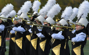 A group of Towson marching band members in black and gold uniforms performing at Fall 2023 events.